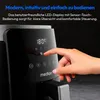 A close-up shot of a hand interacting with the control panel of a black air fryer. Produktbild-Vorschau