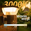 An outdoor wall light with a motion sensor is shown at dusk, with text overlays indicating its features and color temperature. Produktbild-Vorschau