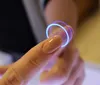 A close-up shot of a person's finger touching a glowing ring. Produktbild-Vorschau