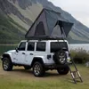 A white Jeep Wrangler with a rooftop tent is parked on a grassy area next to a body of water with mountains in the background. Produktbild-Vorschau