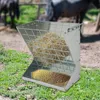 A metal hay feeder filled with hay and grain, placed outdoors on grass with horses in the background. Podgląd zdjęcia produktu