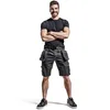 A man wearing work shorts and a t-shirt, standing with his arms crossed. Produktbild-Vorschau