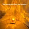 A cube-shaped lamp with a textured surface sits on a round table, casting warm, patterned light onto a textured wall and the table surface. A palm frond casts a shadow on the wall. Produktbild-Vorschau