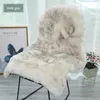 A fluffy sheepskin rug draped over a chair, with a framed picture and potted flowers in the background. Produktbild-Vorschau