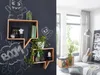 A room with a dark gray wall featuring wooden shelves decorated with plants and chalk drawings, and a bright living area with a window, curtains, a lamp, and furniture. Produktbild-Vorschau