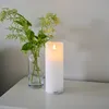 A white LED candle and a vase with green foliage sit on a white surface against a light gray wall. Produktbild-Vorschau