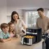 A family is gathered around a kitchen counter, with a woman pouring something into an air fryer basket. Anteprima dell’immagine prodotto