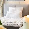 A bed with pillows and a mattress topper, with a candle in the foreground. Produktbild-Vorschau