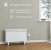 A white electric heater is shown on a wooden floor in front of a grey wall. To the left of the heater, there is a graphic with text highlighting safety features. A window is visible on the right side of the image. Podgląd zdjęcia produktu
