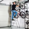A man is using a step ladder to access bicycles mounted on a wall in a garage. Náhľad obrázku produktu