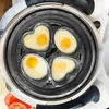 A top-down view of a cooking appliance with four heart-shaped molds containing cooked eggs. Produktbild-Vorschau