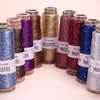 Several spools of glitter yarn are arranged in a semi-circle on a light pink surface. Produktbild-Vorschau