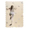 A young girl is climbing on a wooden climbing wall with gray climbing holds. Voir les images du produit