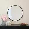 A round black mirror with a metal rim is displayed on a black dresser. To the left of the mirror, a vase of pink roses and a glass are visible. To the right, a decorative object and a bowl of potpourri are placed. Produktbild-Vorschau