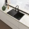A black kitchen sink with a faucet is installed on a white countertop next to a window. Anteprima dell’immagine prodotto