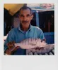 A man holds a fish in front of a market stall. Voir les images du produit