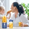 A mother and child are in a kitchen setting, with the mother eating a hot dog and the child looking on. Two portable blenders are on the table, one filled with orange slices and juice. Voir les images du produit