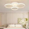 A modern white ceiling lamp with four rings is shown in a bedroom setting above a bed. Podgląd zdjęcia produktu