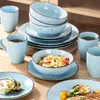 A set of light blue ceramic dishes and mugs are arranged on a wooden table, with some dishes containing food. Náhled obrázku produktu