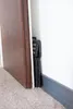 A folded black step stool is tucked between a wooden door and a white wall. Produktbild-Vorschau