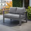 A grey outdoor loveseat with cushions is placed on a tiled patio, with a building and foliage in the background. Produktbild-Vorschau