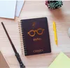 A Harry Potter themed notebook, wand, and pen are laid out on a wooden surface with some papers and a small potted plant. Produktbild-Vorschau