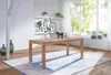 A wooden dining table is set in a bright, airy room with a large window and shelves with plants and pictures. Anteprima dell’immagine prodotto