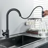 A black kitchen faucet is shown in use, filling a glass pitcher with water. Several white mugs are hanging on a rack nearby. Produktbild-Vorschau