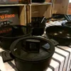 A collection of black cookware, including pots and pans, displayed on a striped tablecloth. Podgląd zdjęcia produktu