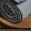 A rolled-up gray fleece blanket with black stitching is placed on a wooden surface. Náhled obrázku produktu