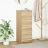 A tall, narrow chest of drawers with five drawers, made of wood-effect material, stands against a white wall. A large green plant in a white pot is to the left, and a coat rack with a beige coat and a white handbag is to the right. A round mirror is visibl Náhled obrázku produktu