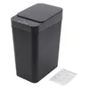A black automatic trash can with its lid closed, placed on a white background. An instruction manual is visible to the right of the trash can. Náhled obrázku produktu