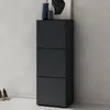 A dark gray shoe cabinet with three drawers stands against a light gray wall. Two pairs of women's shoes are visible on the floor to the left of the cabinet. A framed picture and two decorative vases are on top of the cabinet. Produktbild-Vorschau