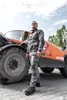 A man in workwear stands in front of a large orange construction vehicle. Produktbild-Vorschau