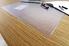 A transparent desk mat with a wood grain pattern is placed on a wooden desk. A laptop, glasses, and pens are visible on the mat. Produktbild-Vorschau