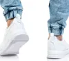 A close-up shot of a person's legs wearing white Puma sneakers and acid-washed jeans. Anteprima dell’immagine prodotto