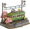 A 3D wooden model of a train station with a green train, cherry blossom trees, and overhead power lines. Produktbild-Vorschau