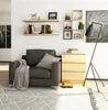 A modern living room scene with a dark gray armchair, a wooden chest of drawers, shelves with books and decor, and a floor lamp. Anteprima dell’immagine prodotto