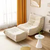 A beige armchair and ottoman are placed in a room with yellow curtains and a small white side table. Náhled obrázku produktu