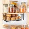 A kitchen shelf with various food items stored in jars and a hanging basket filled with potatoes. Produktbild-Vorschau