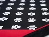 A close-up view of a dog bed with a pattern of white paw prints on a black background, and a red trim along the bottom edge. Náhled obrázku produktu