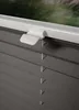 Close-up of a dark gray pleated blind with a white clamp mechanism attached to the top. Produktbild-Vorschau