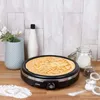 A crepe maker with a crepe on it, surrounded by ingredients and kitchenware. Podgląd zdjęcia produktu