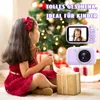 A young girl in a red dress is sitting on the floor, opening a gift box next to a Christmas tree. Two digital cameras are shown in the upper right corner of the image. Produktbild-Vorschau