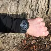 A person's arm wearing a black G-Shock watch is resting against a textured tree trunk. Produktbild-Vorschau