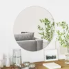 A round mirror reflecting a sofa and a plant, placed on a wooden table with decorative items. Náhľad obrázku produktu