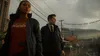 Two people, a woman and a man, are walking down a street in what appears to be a small town. The weather is overcast and it looks like it might have rained recently. There are buildings and trees visible in the background. Podgląd zdjęcia produktu