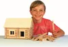 A young boy is smiling and holding a wooden building stick next to a partially constructed wooden log cabin model. Anteprima dell’immagine prodotto