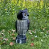 A solar-powered owl decoy stands in a grassy area with yellow flowers in the background. Náhľad obrázku produktu