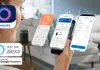 A person's face and hand are visible in the foreground, holding a smartphone displaying smart home app interfaces. The background shows a blurred living room setting with a smart speaker. Podgląd zdjęcia produktu